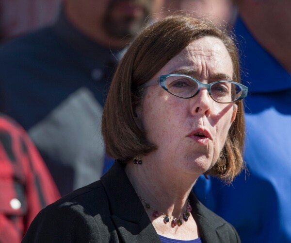 brown in a black jacket and blue top and necklace