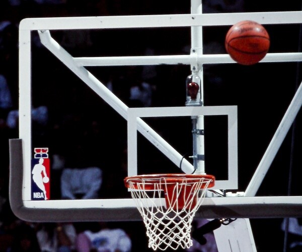 basketball being thrown into a hoop with nba logo on the backboard