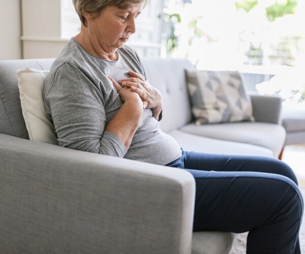 woman on couch holding chest in pain