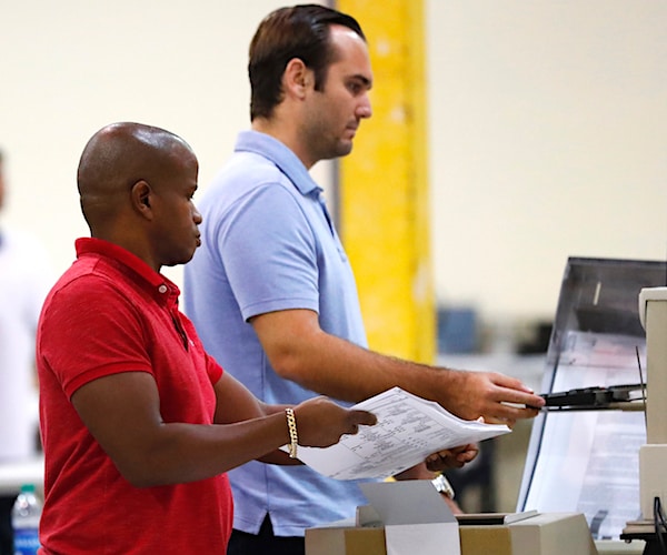 election employees feed ballots through a machine as they count votes