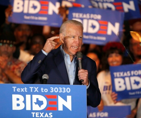 joe biden at a campaign rally with people in the crowd holding texas for biden signs behind him