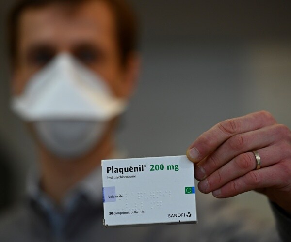 pharmacist wearing a face mask holds up a small box labeled plaquenil 200 mg