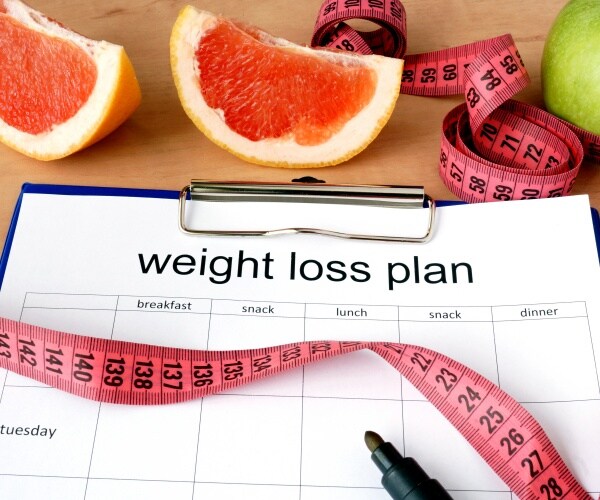 clipboard with paper that says 'weight-loss plan' and a measuring tape and some fruit