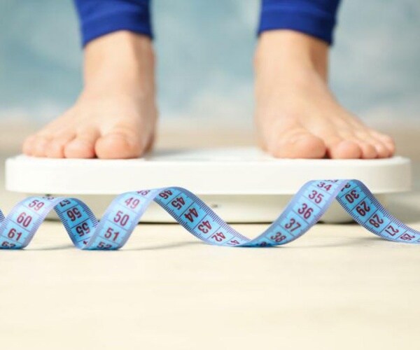 women's feet on scale, measuring tape on floor