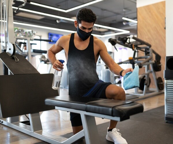 man cleaning exercise machine in gym after using it