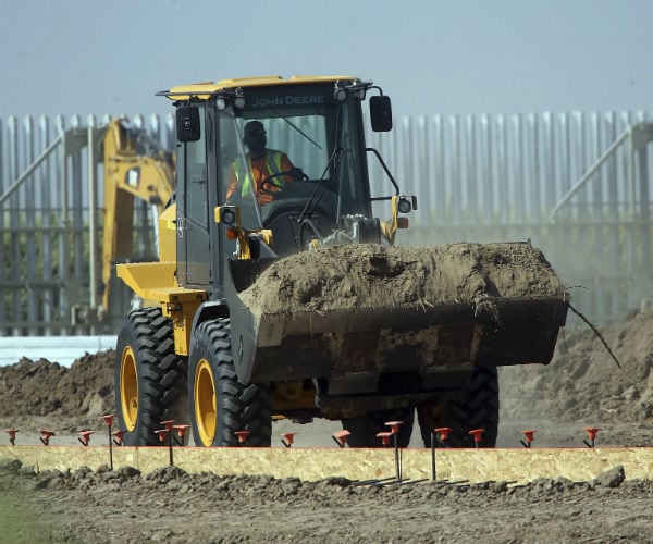 Heavy equipment moves dirt as the steel bollards are seen in the background during construction of the wall in Texas.