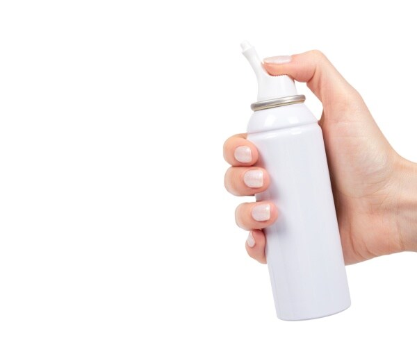 a hand spraying a white bottle of saline spray on white background