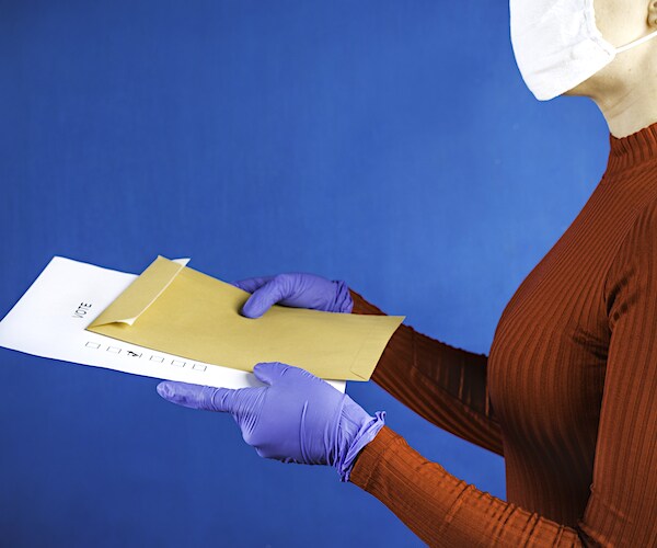 a woman wearing a face mask carries a vote by mail