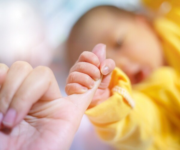 baby wearing yellow holds the pinky finger of a woman