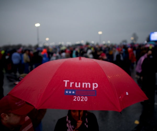 woman holding an umbrella that says trump 2020 on it outside a campaign rally