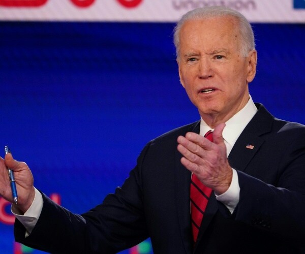 joe biden in a black suit and red striped tie speaking on the democratic debate stage 