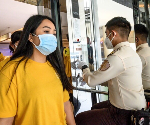 woman wearing a yellow shirt and blue mask enters and elevator with a man operating it in uniform