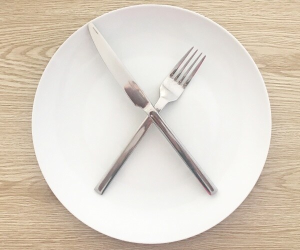 empty white dinner plate with a fork and knife over each other shaped like an 'x'