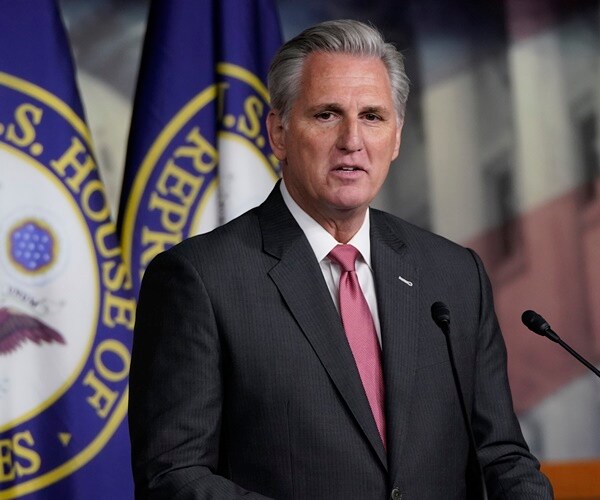 kevin mccarthy stands in front of house of representative flags