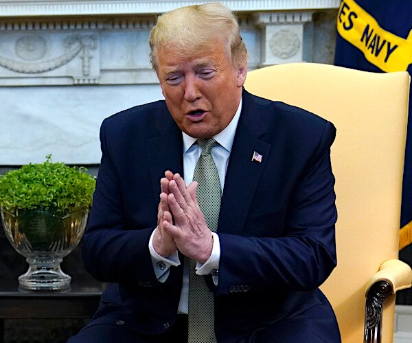 president donald trump strikes a pose of prayer in the oval office.