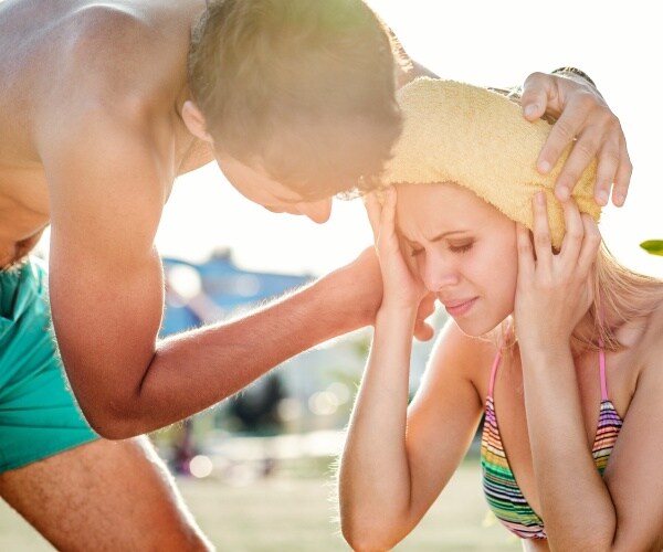 man and woman at beach in bathing suits, man putting cold compress on woman's head