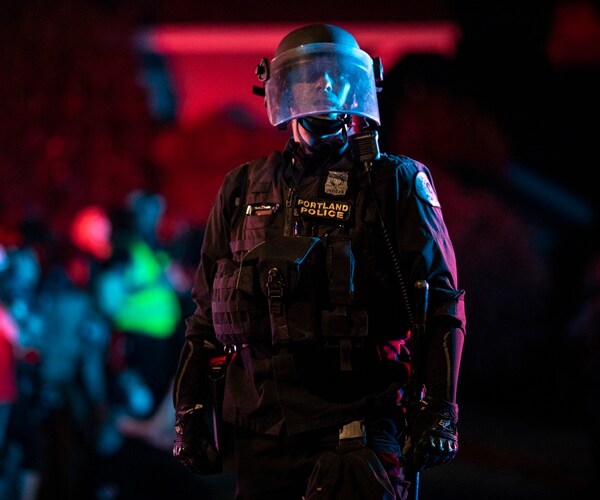 a portland police officer stands in full gear against a red lit night background