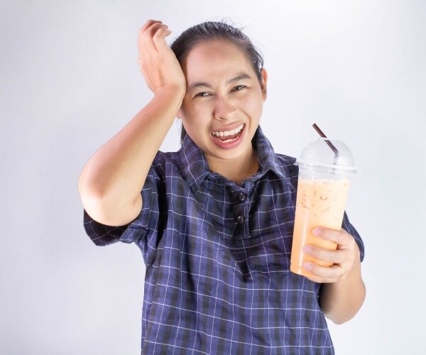 woman drinking cold drink, with hand to head due to painful 'brain freeze'