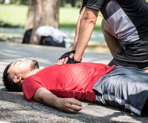 Man giving CPR to man on ground outside