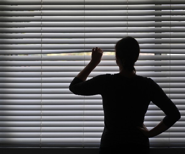 a woman peeking out of window blinds