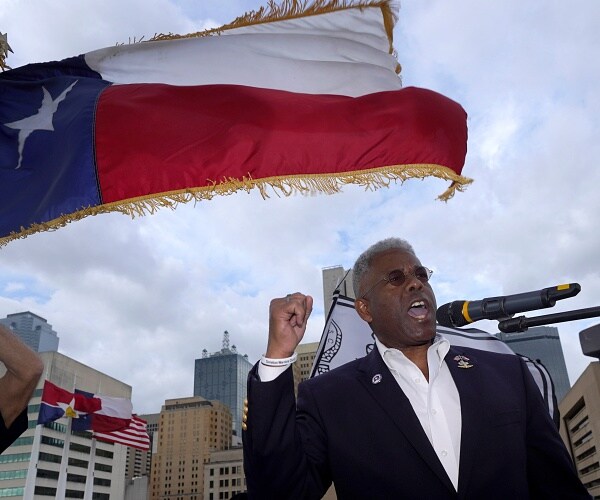 allen west speaks into mic under texas flag