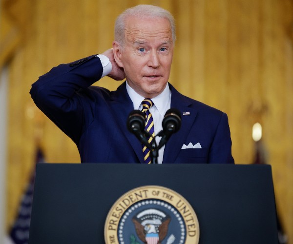 joe biden at the podium with his hand behind his neck