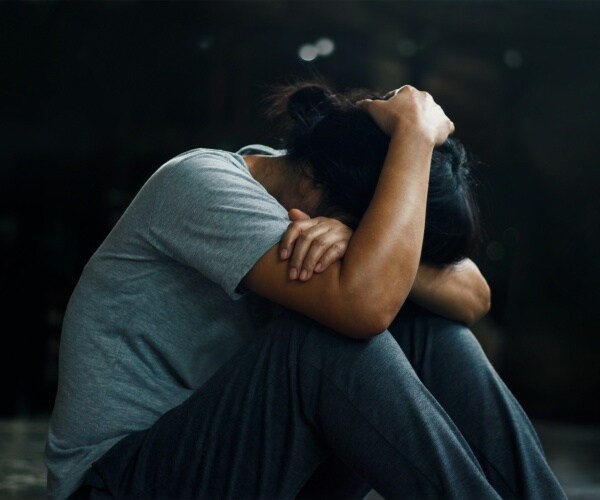 woman sitting on floor with head in her hands, suffering from PTSD