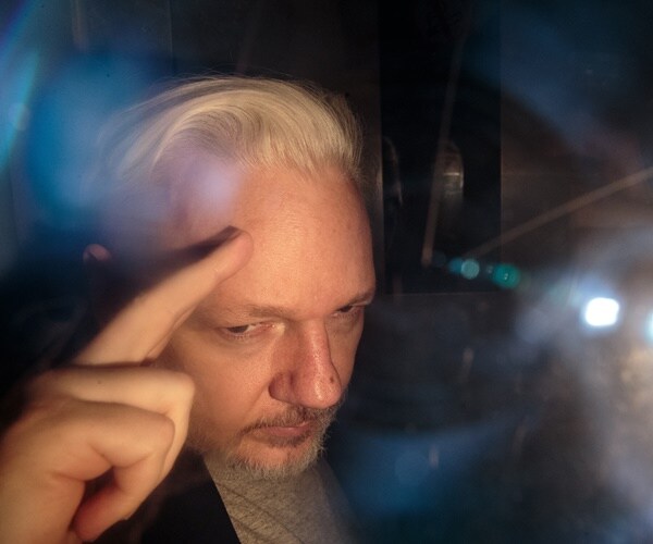 julian assange is seen through glass,, saluting