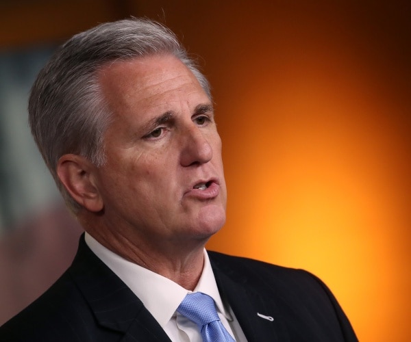 mccarthy in a black suit and blue tie with orange background