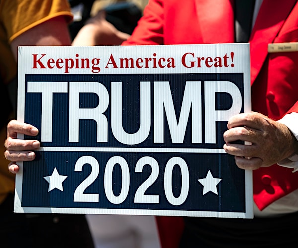 an elderly woman holds a trump 2020 keeping america great banner