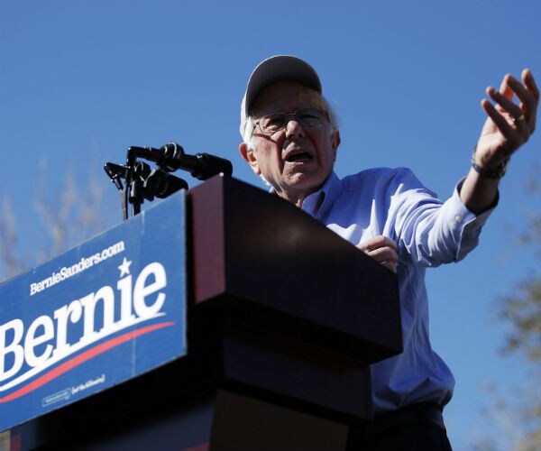 bernie sanders speaking at podium displaying his campaign sign