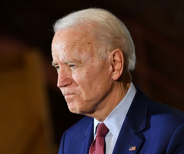 joe biden in a suit and burgundy tie with a brown background