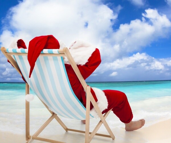 man in Santa costume sitting in chair on warm beach