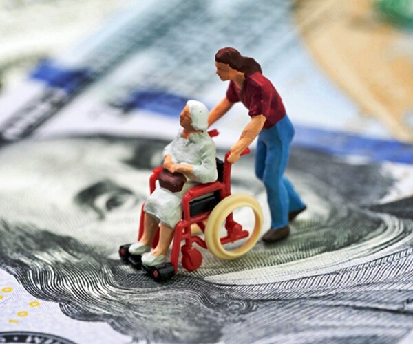 elderly woman pushed in wheelchair across face of us currency dollar bill