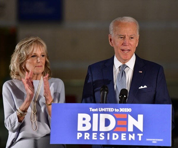 joe biden stands at a podium with jill biden, applauding next to him