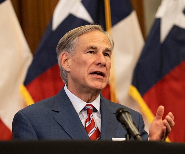 greg abbott stands in front of flags and speaks