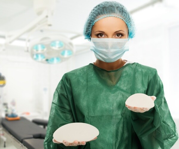 surgeon in scrubs holding two breast implants