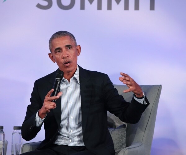 obama in a suit and striped shirt speaking into a mic sitting in a gray armchair