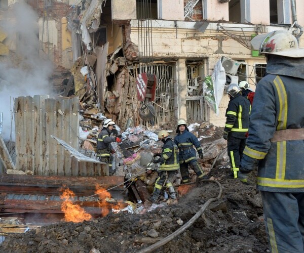 Firemen work to clear the rubble and extinguish a fire by a heavily damaged building