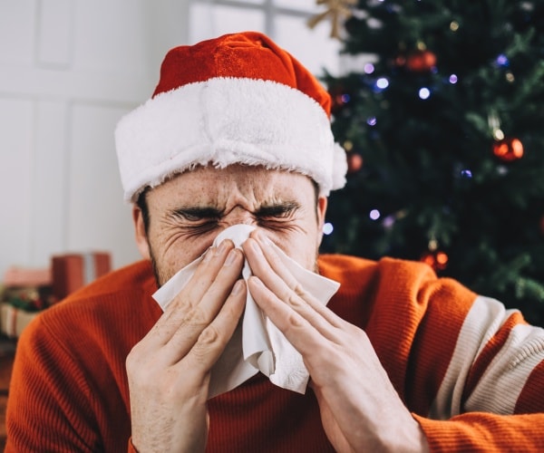 man blowing nose in front of Christmas tree