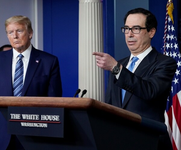 steven mnuchin in a suit and blue tie points to someone at a press briefing with trump