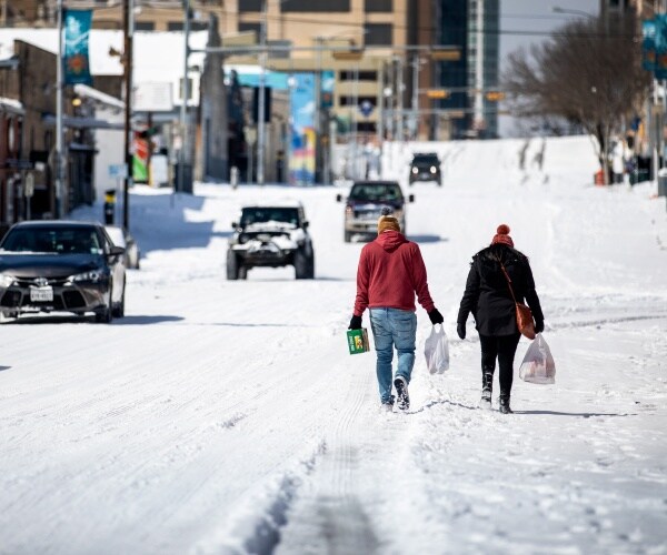 people carry groceries in the snow with cars driving by