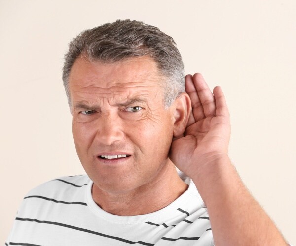 man with hand to ear because having trouble hearing