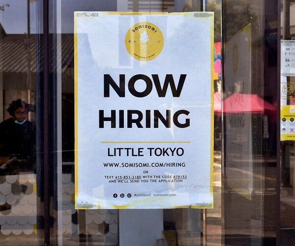 now hiring sign hangs in window