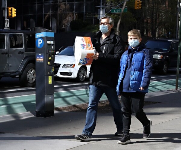 A man carries a package of toilet paper while wearing a protective mask with a boy also wearing a protective mask