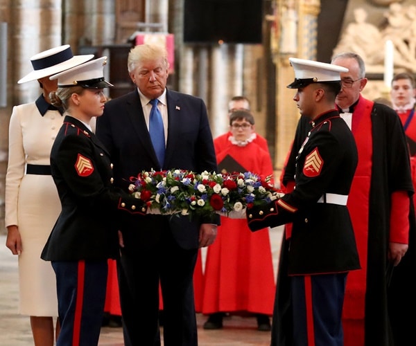 president trump stands in a church watching soldiers lay a wreath at a grave.