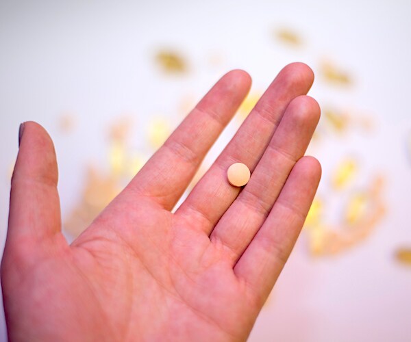 a person holding a yellow multivitamin tablet