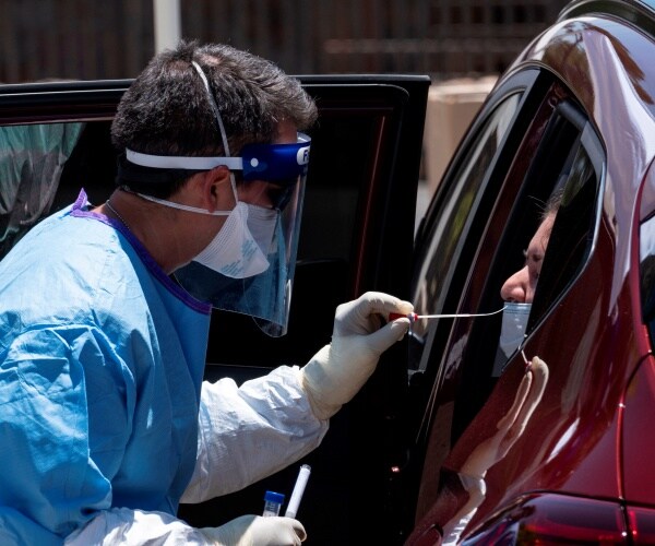 man in blue protective suit mask and white gloves puts a swab in the nose of a person inside a van