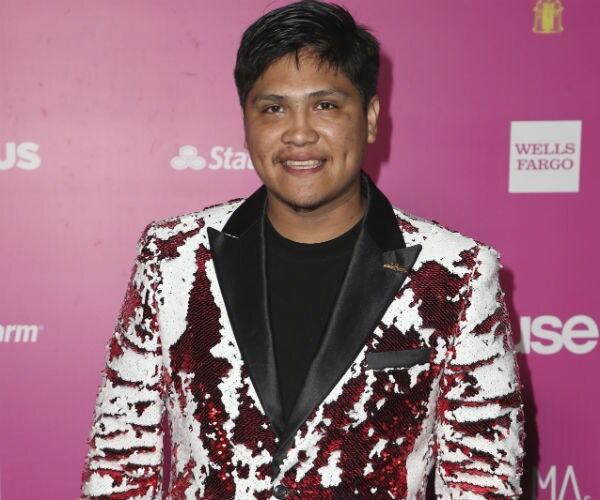 actor johnny ortiz is seen in a floral red, white and black jacket, black shirt and white slacks