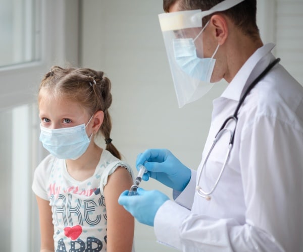 young girl wearing mask and looking nervous as she gets her COVID vaccine